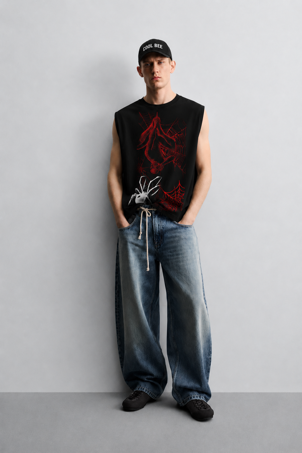 Black tank top with a red-lined illustration of a masked superhero figure hanging upside down in a web, alongside a white spider graphic and red spiderweb accents.