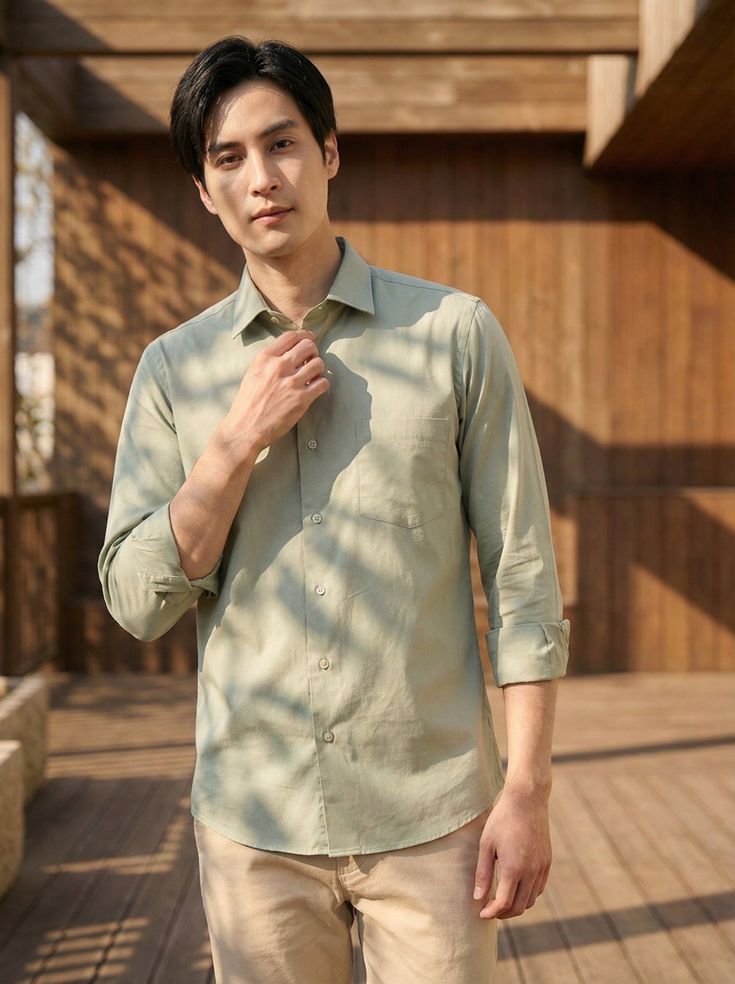 Man wearing a light green shirt standing outdoors with wooden architecture in the background www.coolbeestore.com