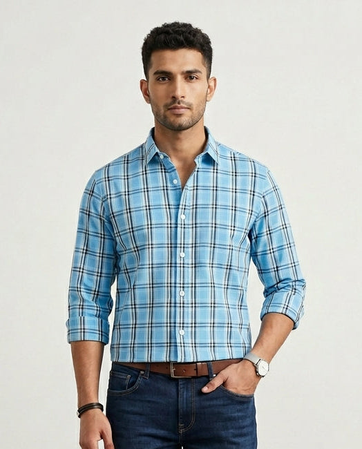 Man wearing a blue plaid shirt and dark jeans against a plain background