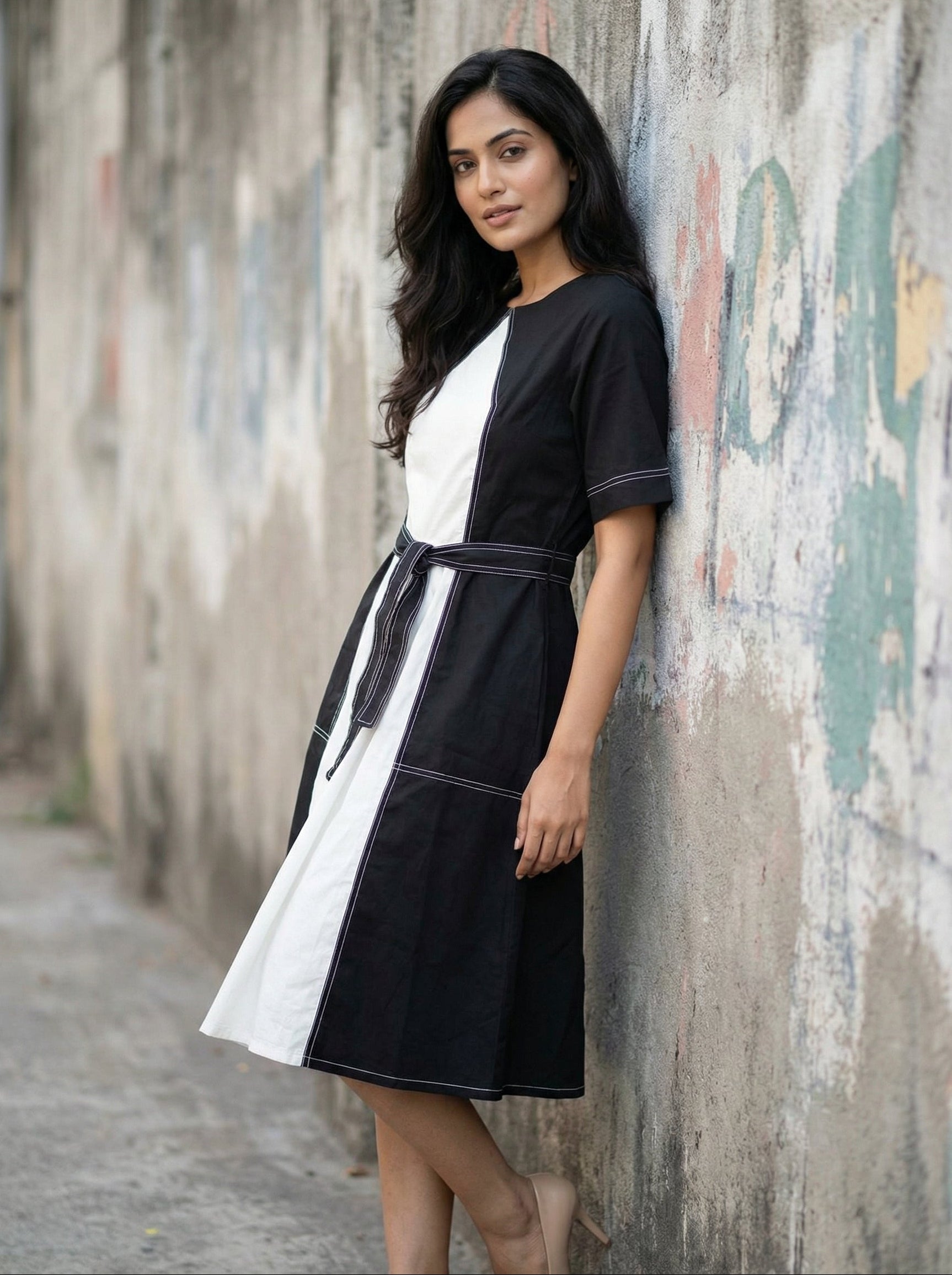 Woman wearing a black and white dress leaning against a textured wall. www.coolbeestore.com