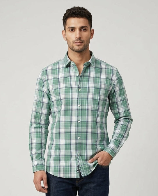 Man wearing a green and white checkered shirt with dark jeans on a light gray background