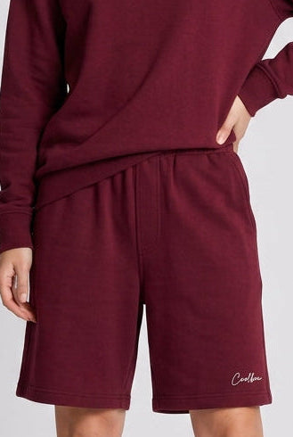 Person wearing a burgundy sweatshirt and shorts set with white socks and shoes on a light gray background