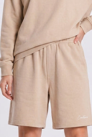 Person wearing a beige sweatshirt and shorts set with white sneakers on a light gray background